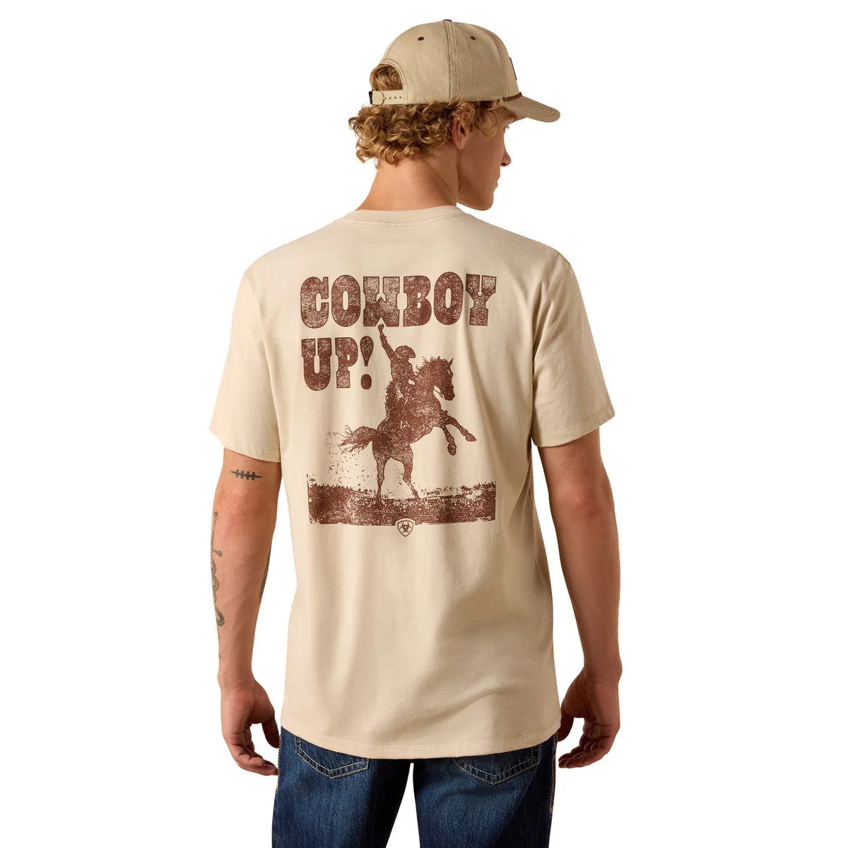 A man wearing a beige t-shirt with a brown distressed graphic on the back that reads 'COWBOY UP!' with a cowboy riding a bucking horse, paired with a matching beige baseball cap and blue jeans, shown from the back against a white background.