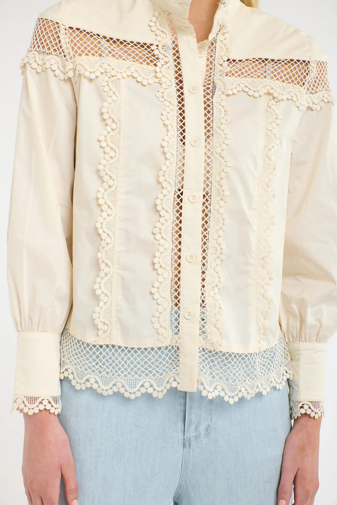 Close up of a woman wearing a 365 Women's Victoria Blouse. Vanilla lace-trimmed with light blue jeans on a white backgrouund