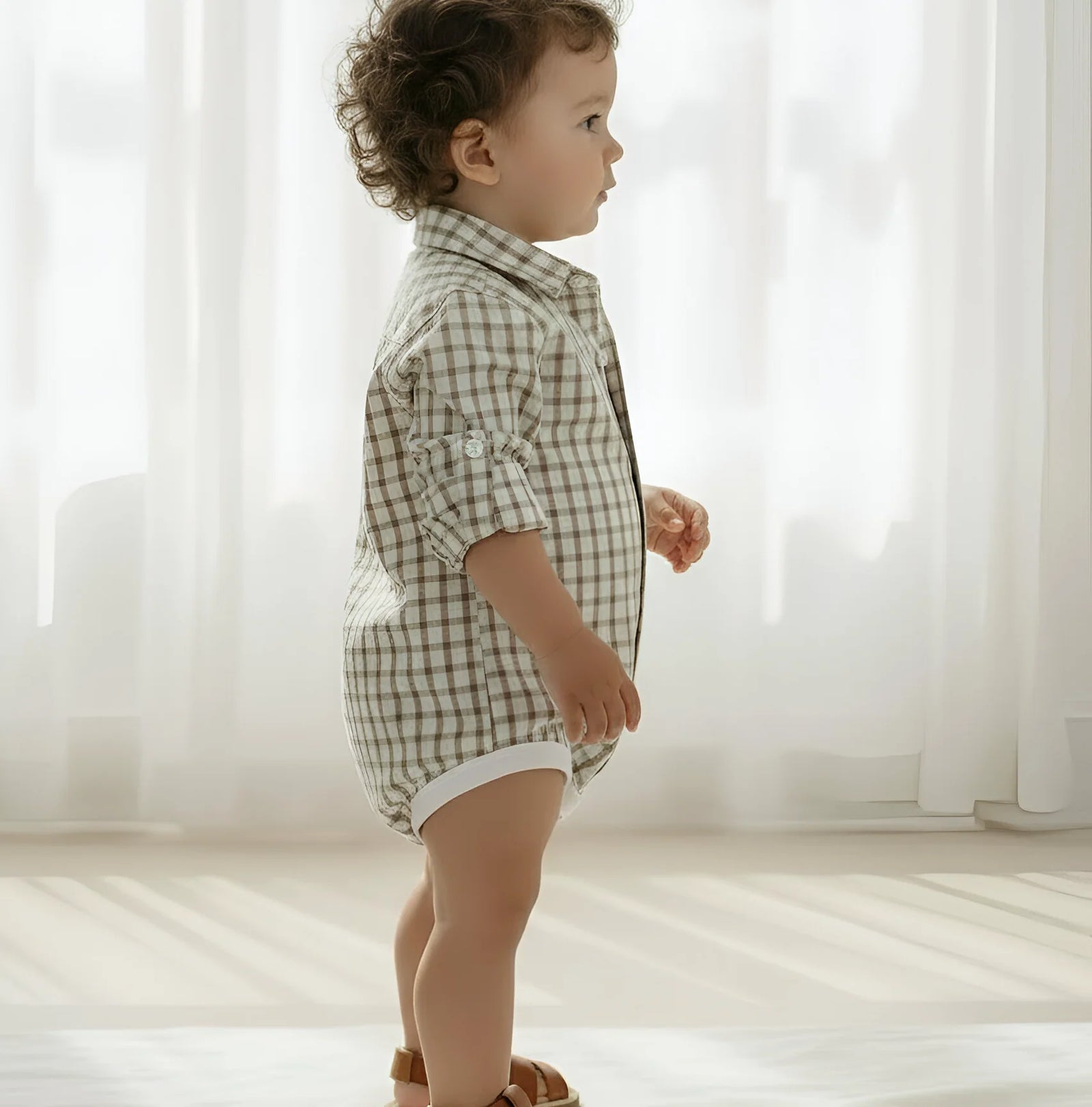 Child wearing a checkered shirt and shorts standing in a softly lit room.