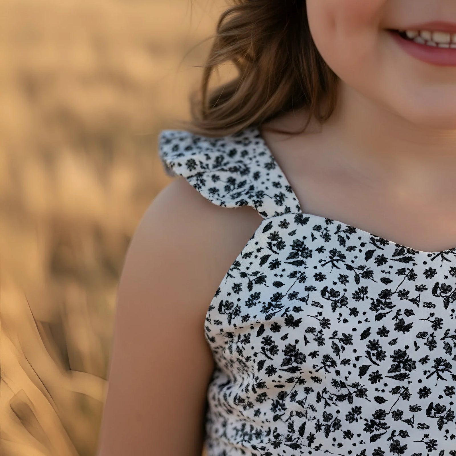 Child wearing a black floral dress in a field of tall grass