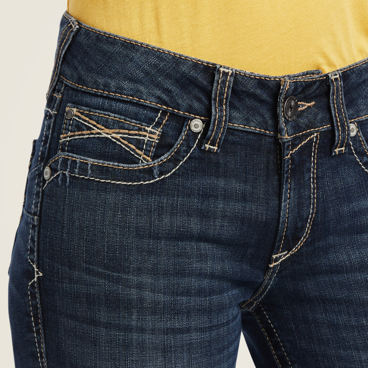 Ariat Women's Lexie Perfect Rise Boot Cut Jean. Close-up of blue jeans with a beige background