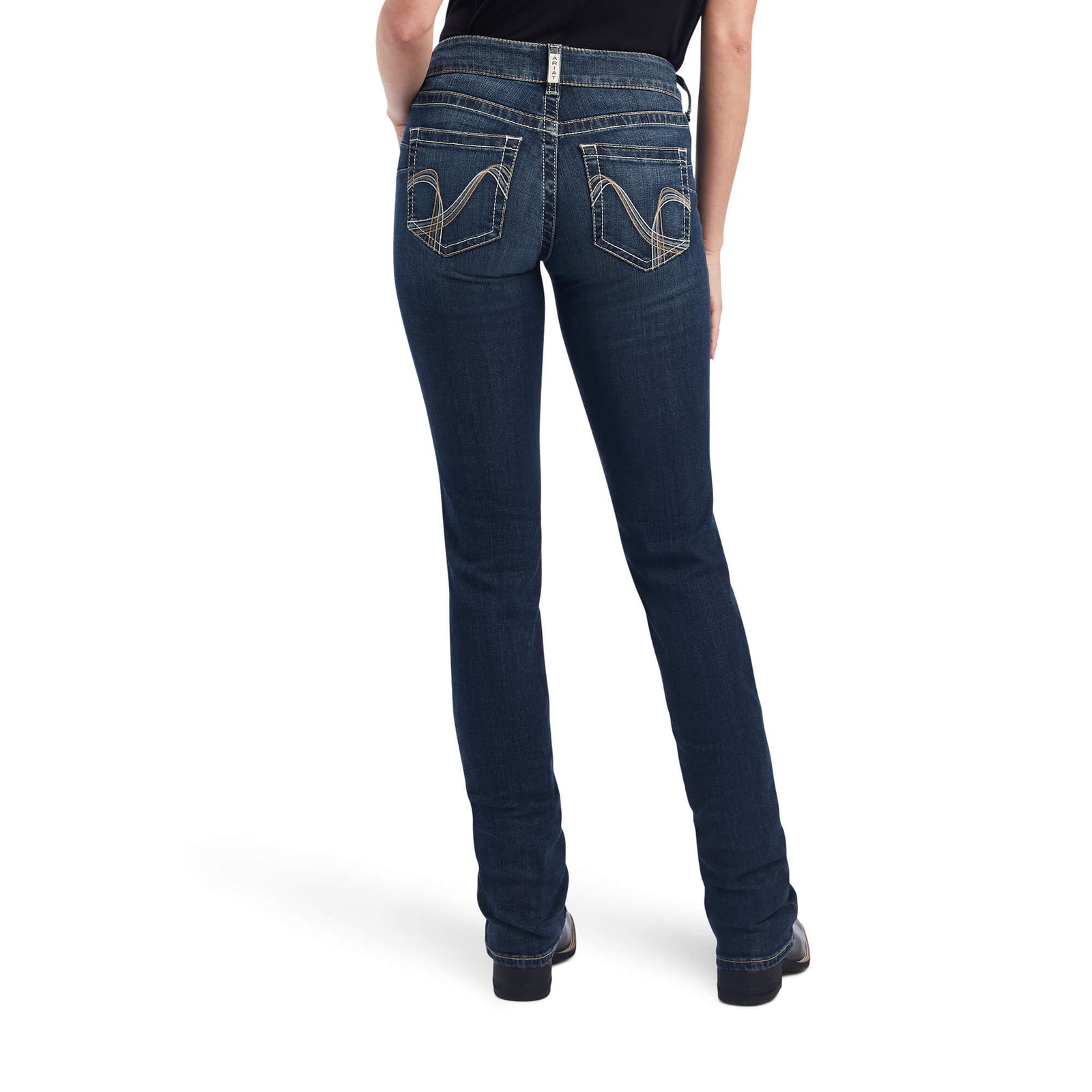 Ariat Women's Freesia Straight Leg Jean. A woman standing and facing the front, wearing mid-rise straight leg blue jeans and black boots.