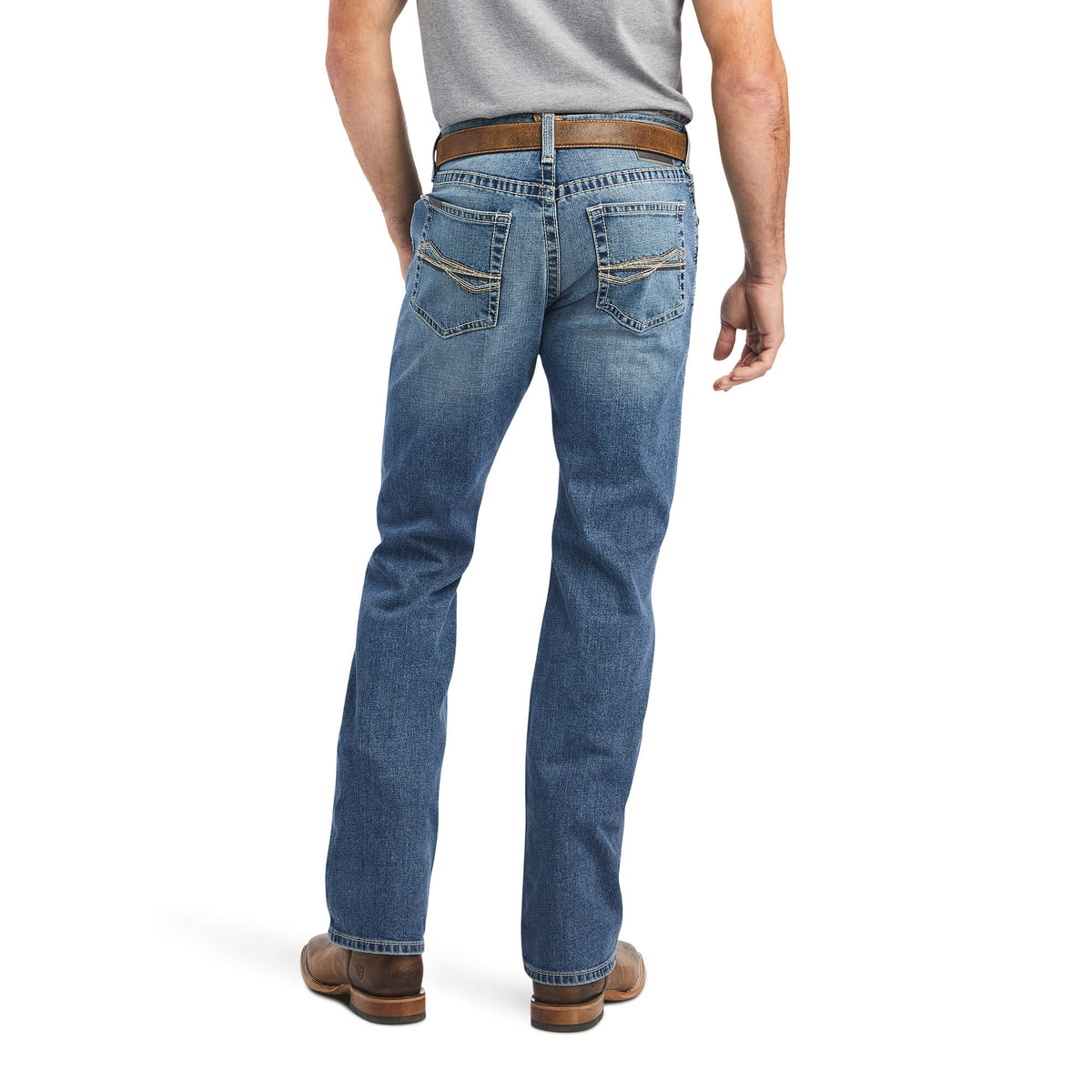 Ariat Men's M5 Bauer Straight Leg Jean. A man viewed from the back wearing blue straight leg jeans with a belt and tan cowboy boots.
