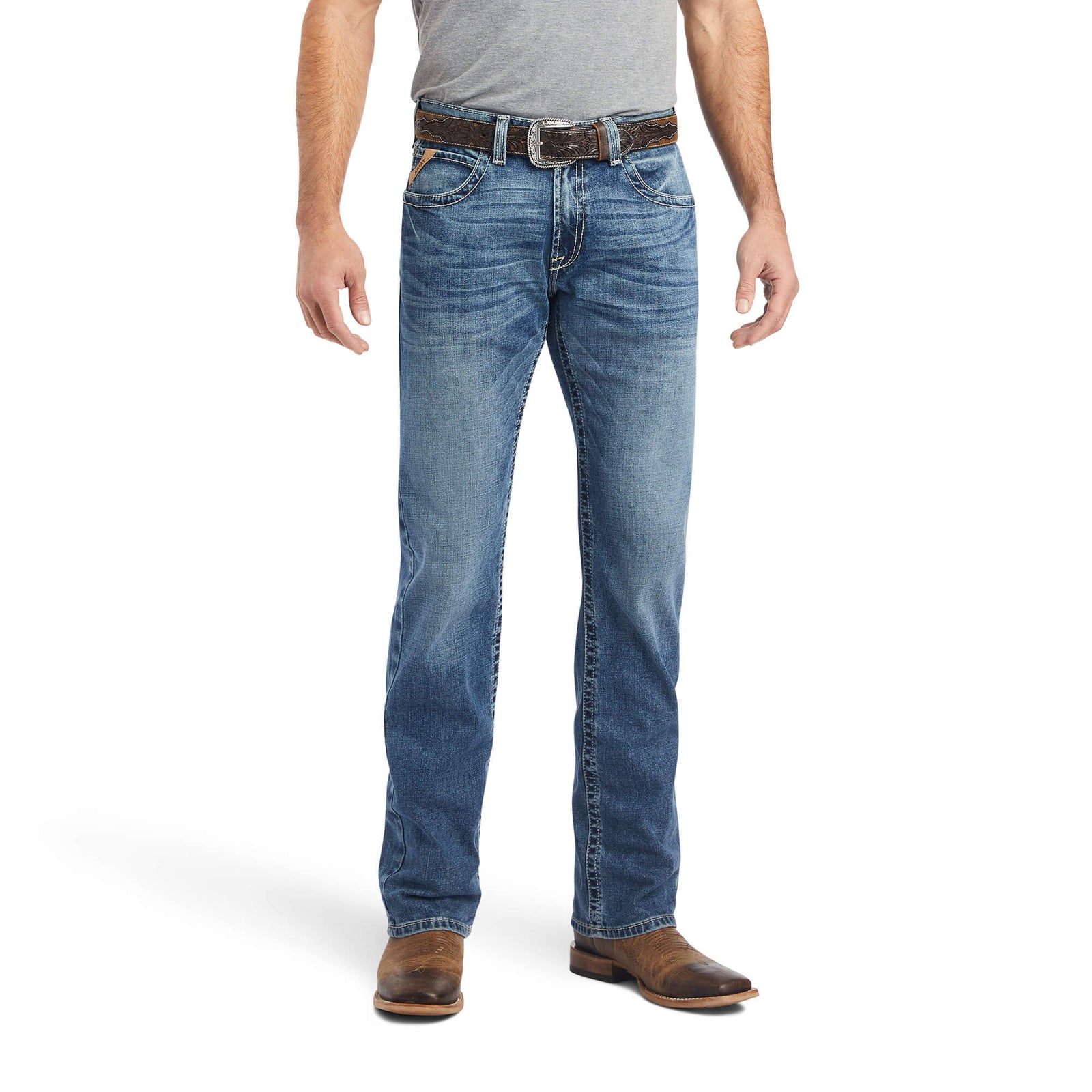 A man standing straight, wearing Ariat Men's M5 Bauer Straight Leg Jean, a belt, and shoes, with his hands in his pockets.