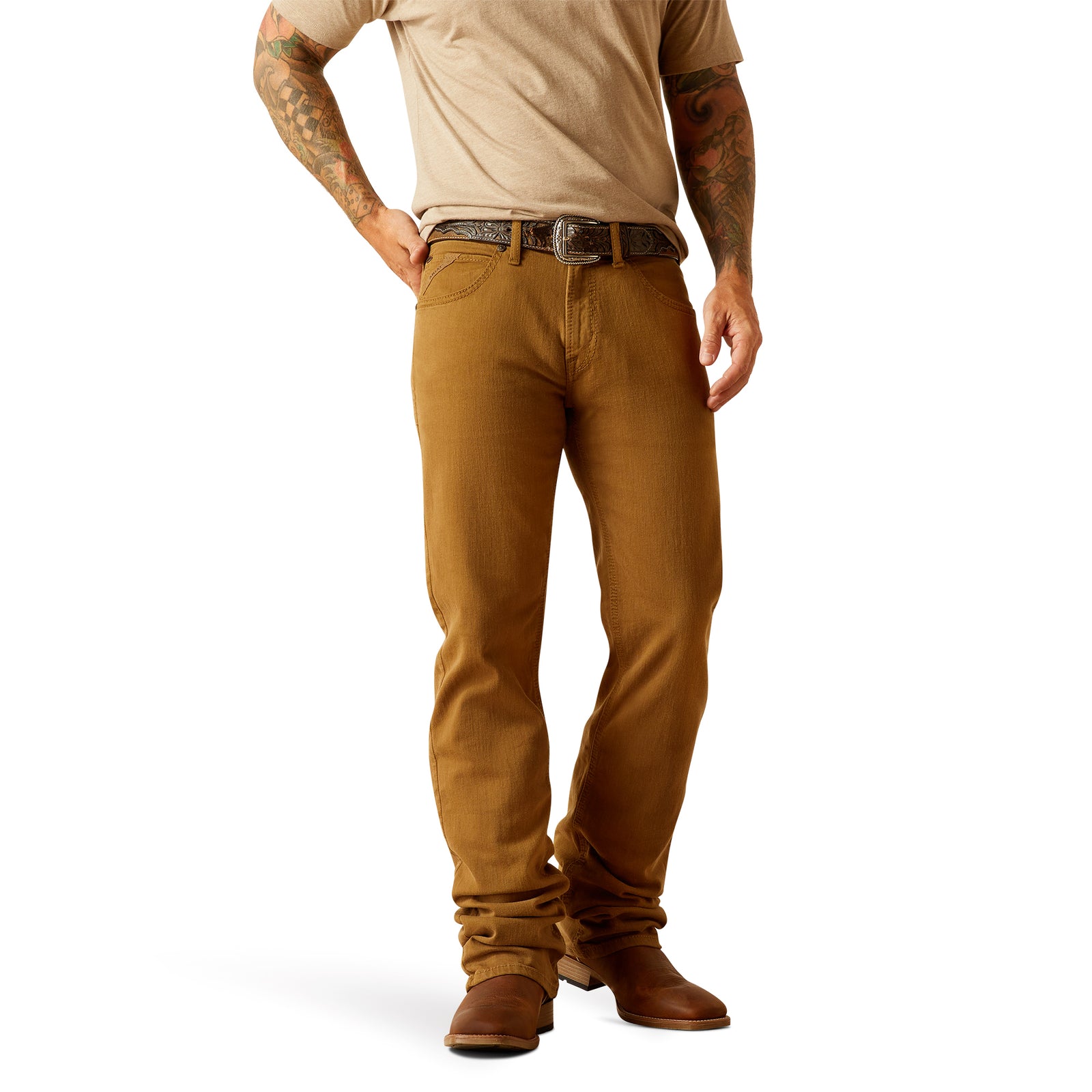 Ariat Men's M5 Hansen Straight Leg Jean. A man wearing brown straight leg jeans and brown cowboy boots, with a visible tattoo on the upper left arm.