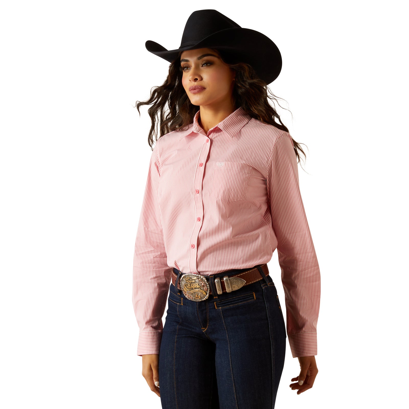 Ariat Women's Kirby L/S Western Shirt. A woman wearing a pink long-sleeved western shirt with a round neckline and a single chest pocket, paired with blue jeans and a brown cowboy hat.