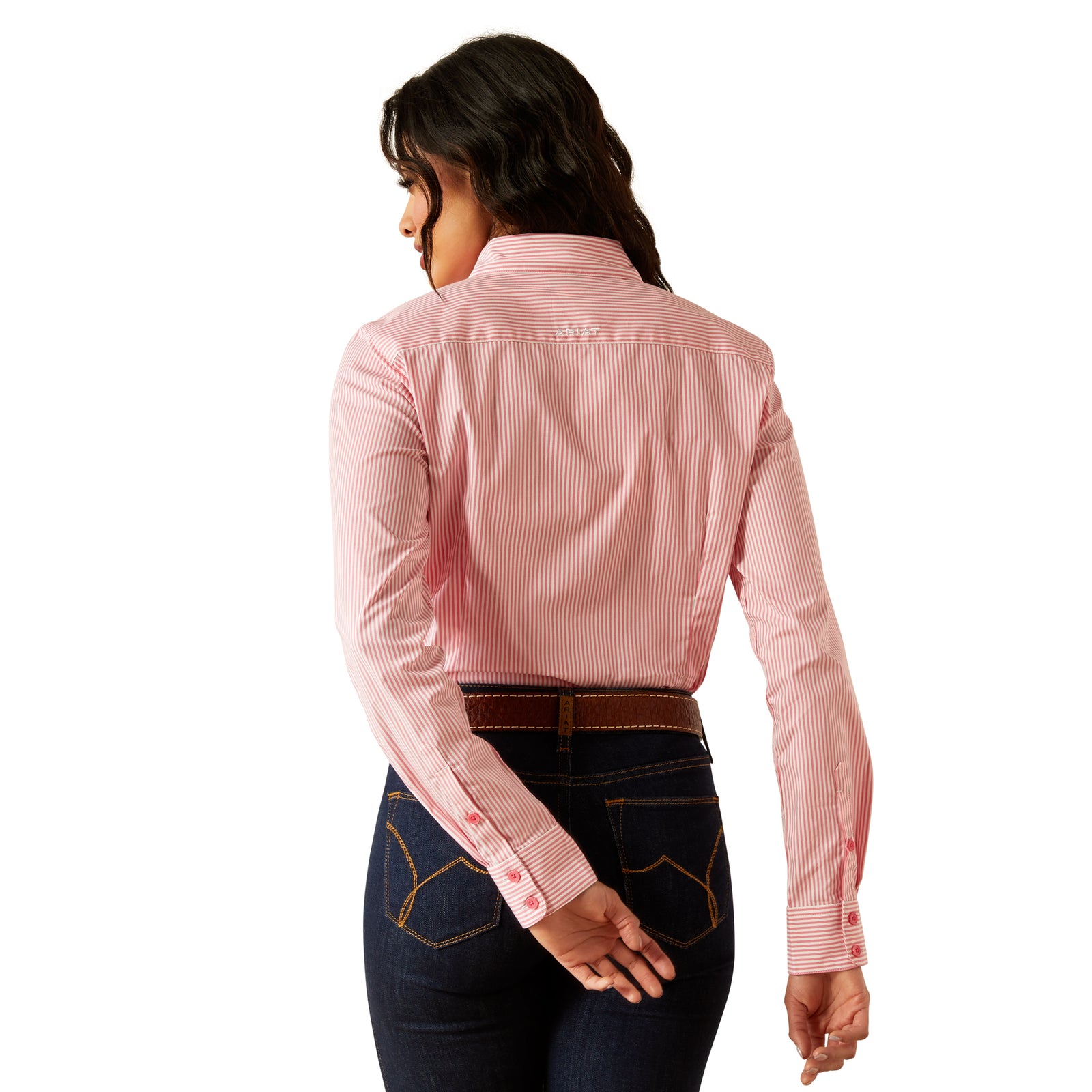 Ariat Women's Kirby L/S Western Shirt. A woman wearing a pink long-sleeved western shirt with a round neckline and a single chest pocket, paired with blue jeans and a brown cowboy hat.