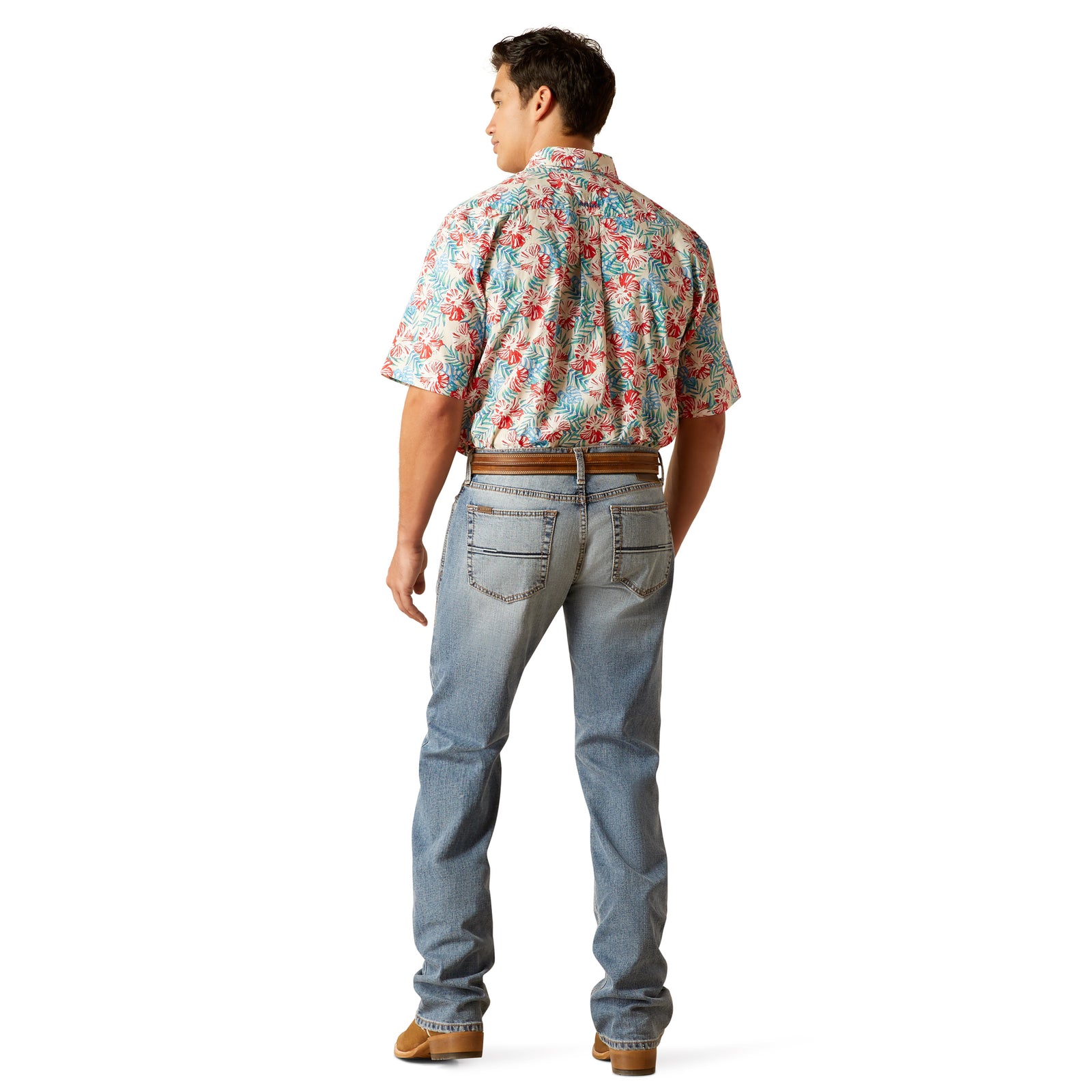 A man wearing a pair of Ariat M7 Deco Men's Straight Leg Jeans, which are slim through the seat and thigh with a low rise and straight leg opening. He is also wearing a floral shirt and brown shoes.