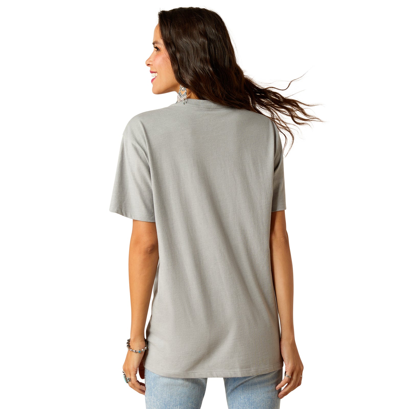Ariat Women's Day and Night S/S Tee. A woman wearing a gray Ariat brand T-shirt with a graphic print, paired with blue jeans and a belt.