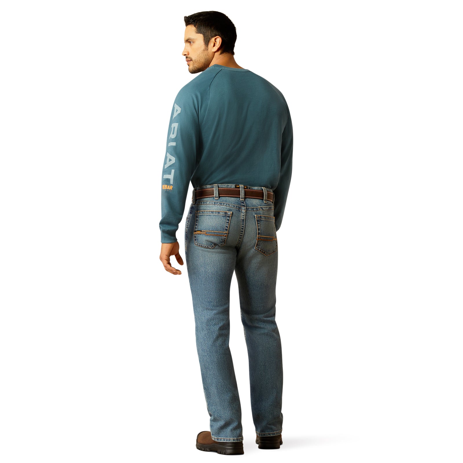 A man standing wearing Ariat Men's Rebar M7 Rail Slim Straight Jean, a blue denim jean with a slim fit and a straight leg cut.