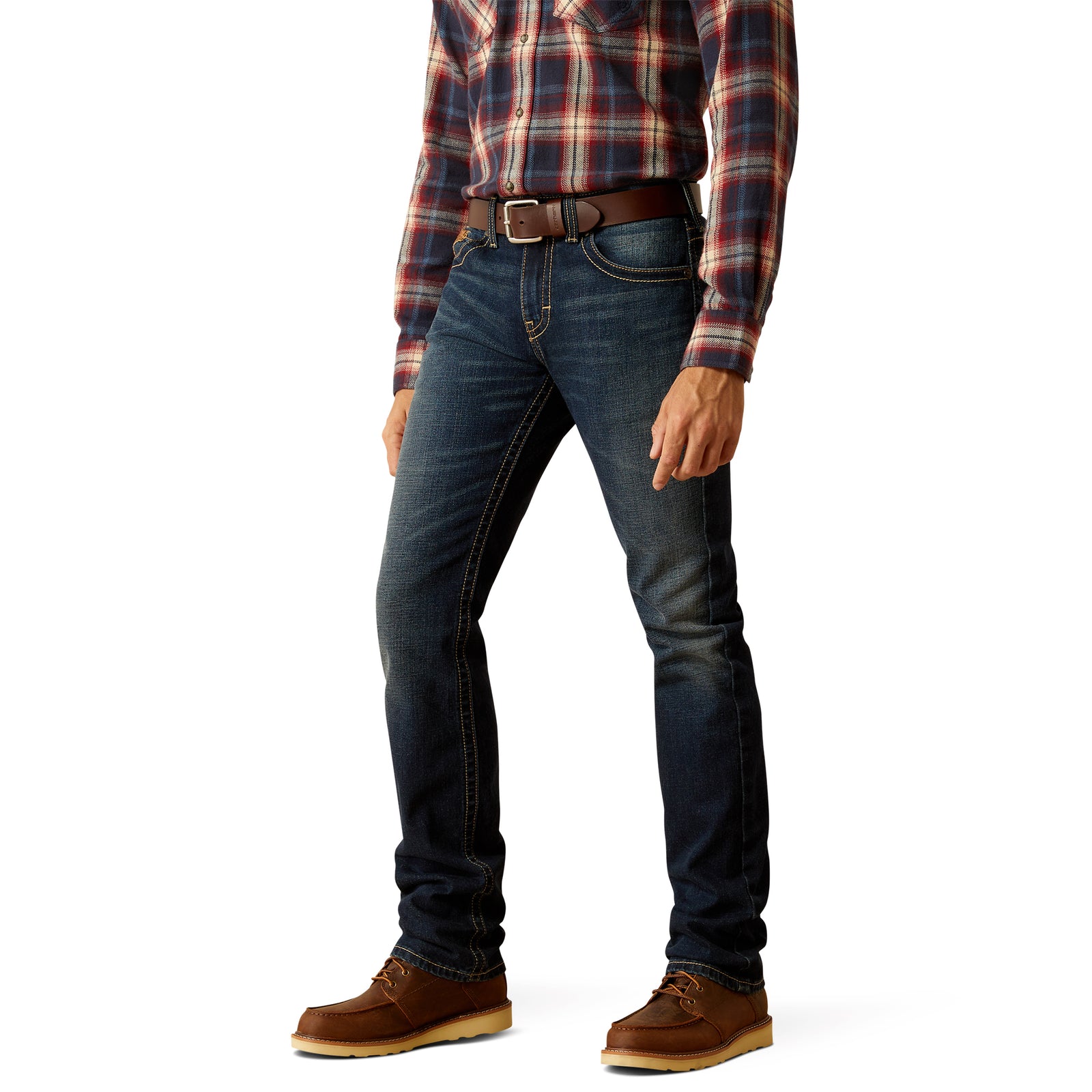 Ariat Men's M8 Modern Gunner Slim Leg Jean. A man standing side-on wearing a plaid shirt, belt, and brown shoes, paired with slim-fit blue jeans.