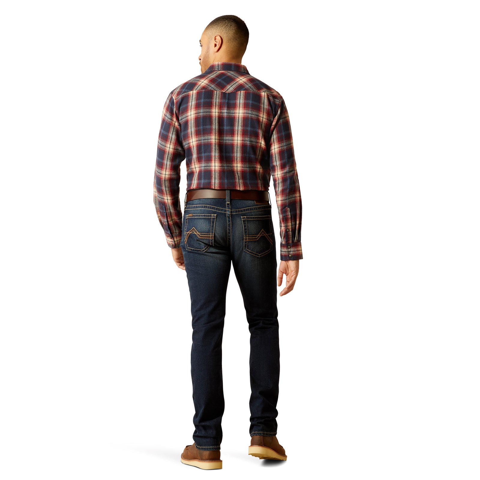 Ariat Men's M8 Modern Gunner Slim Leg Jean. A man standing side-on wearing a plaid shirt, belt, and brown shoes, paired with slim-fit blue jeans.