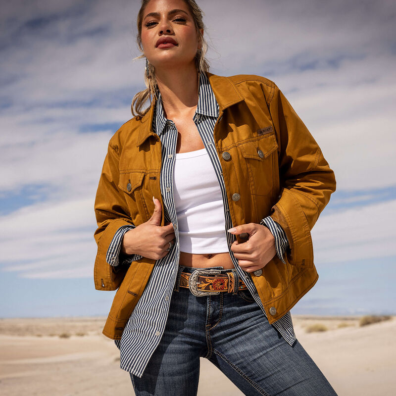 Woman wearing a mustard jacket, white top, and blue jeans in a desert setting