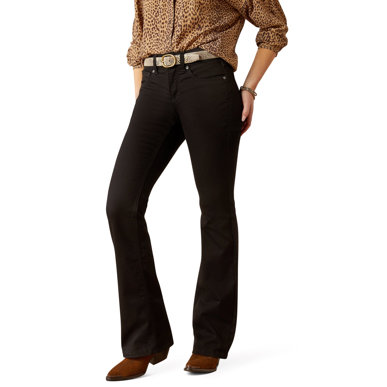 A woman standing, wearing Ariat Women's Perfect Rise Ella Boot Cut Jean, a black belt, and brown boots.