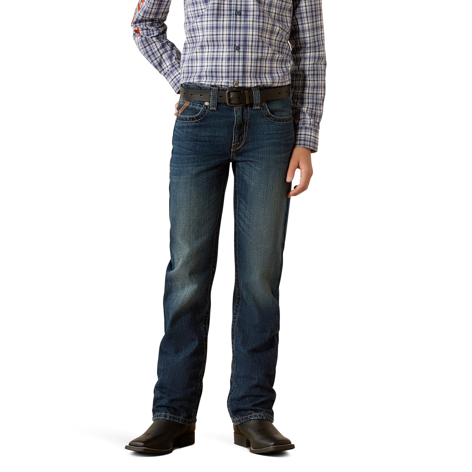 Ariat Boy's B5 Slim Nate Straight Leg Jean. A boy standing with hands in pockets, wearing a plaid shirt, a belt, and boots, with a pair of slim fit blue denim jeans.