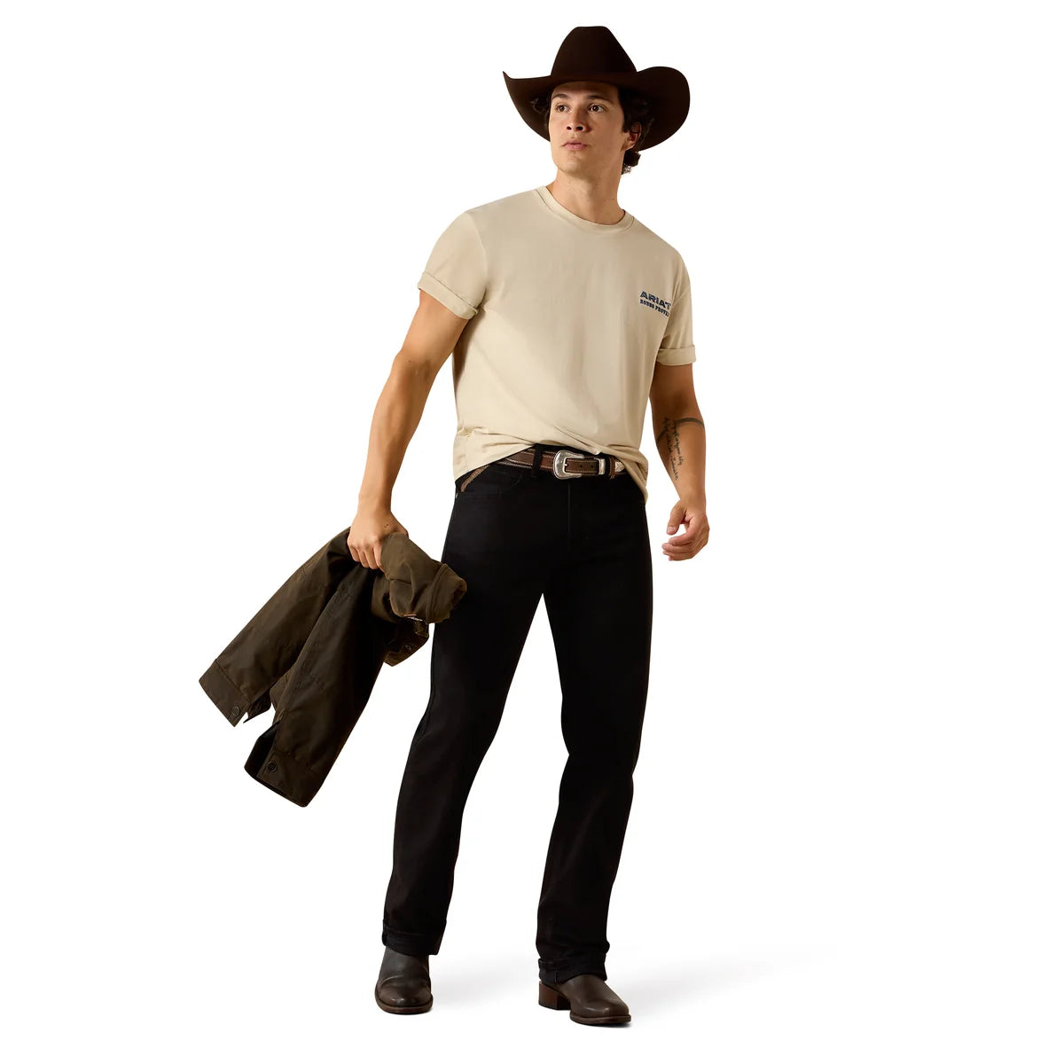Man wearing a beige t-shirt, black pants, and a cowboy hat holding a jacket on a white background