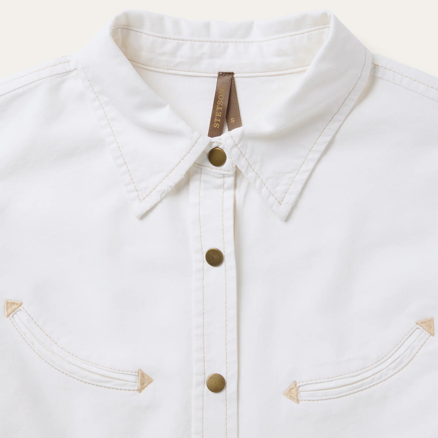 Close-up of a white denim jacket with gold buttons on a light gray background