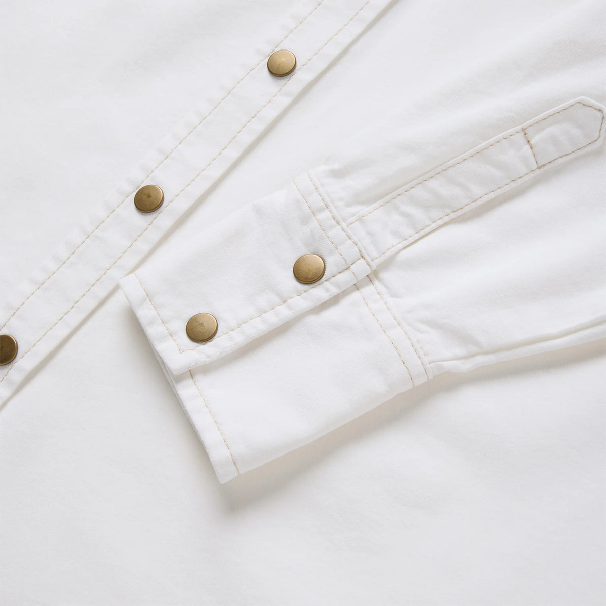Close-up of a white denim jacket with gold buttons on a light gray background