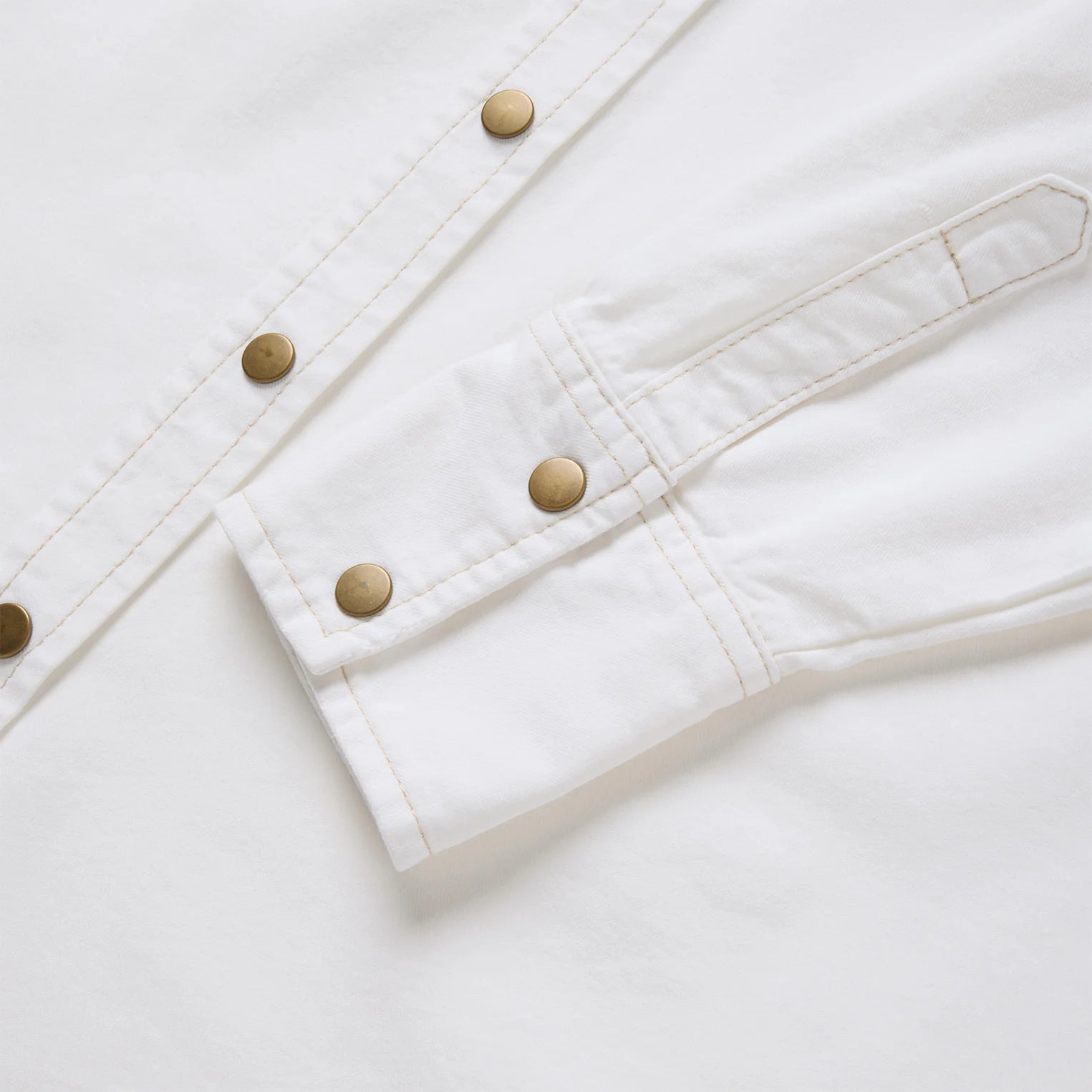 Close-up of a white denim jacket with gold buttons on a light gray background