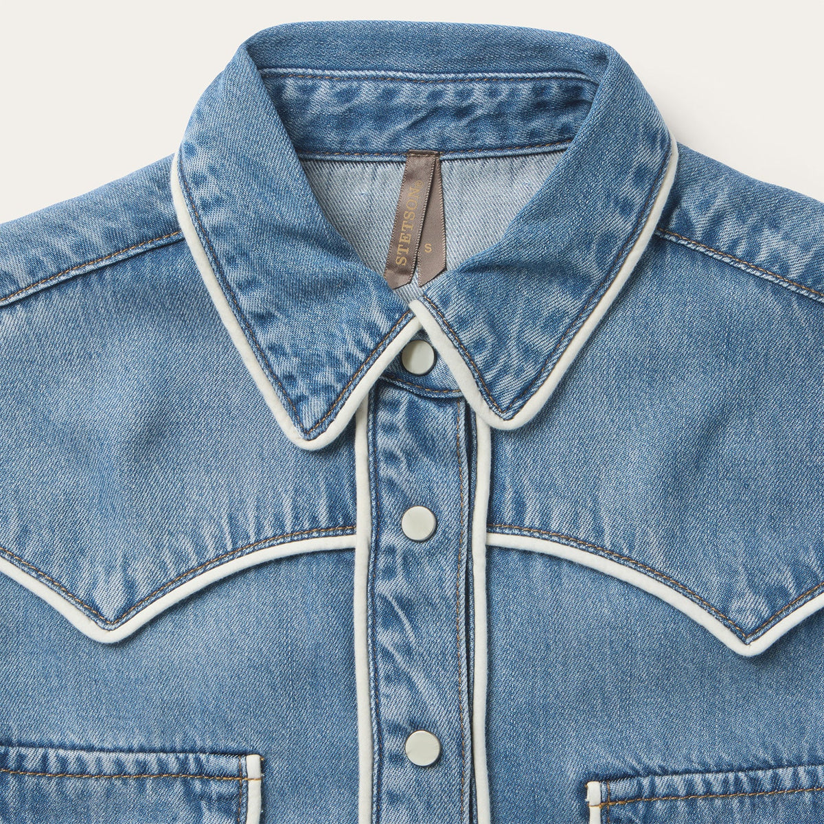 Close-up of a blue denim jacket with white trim on a light gray background
