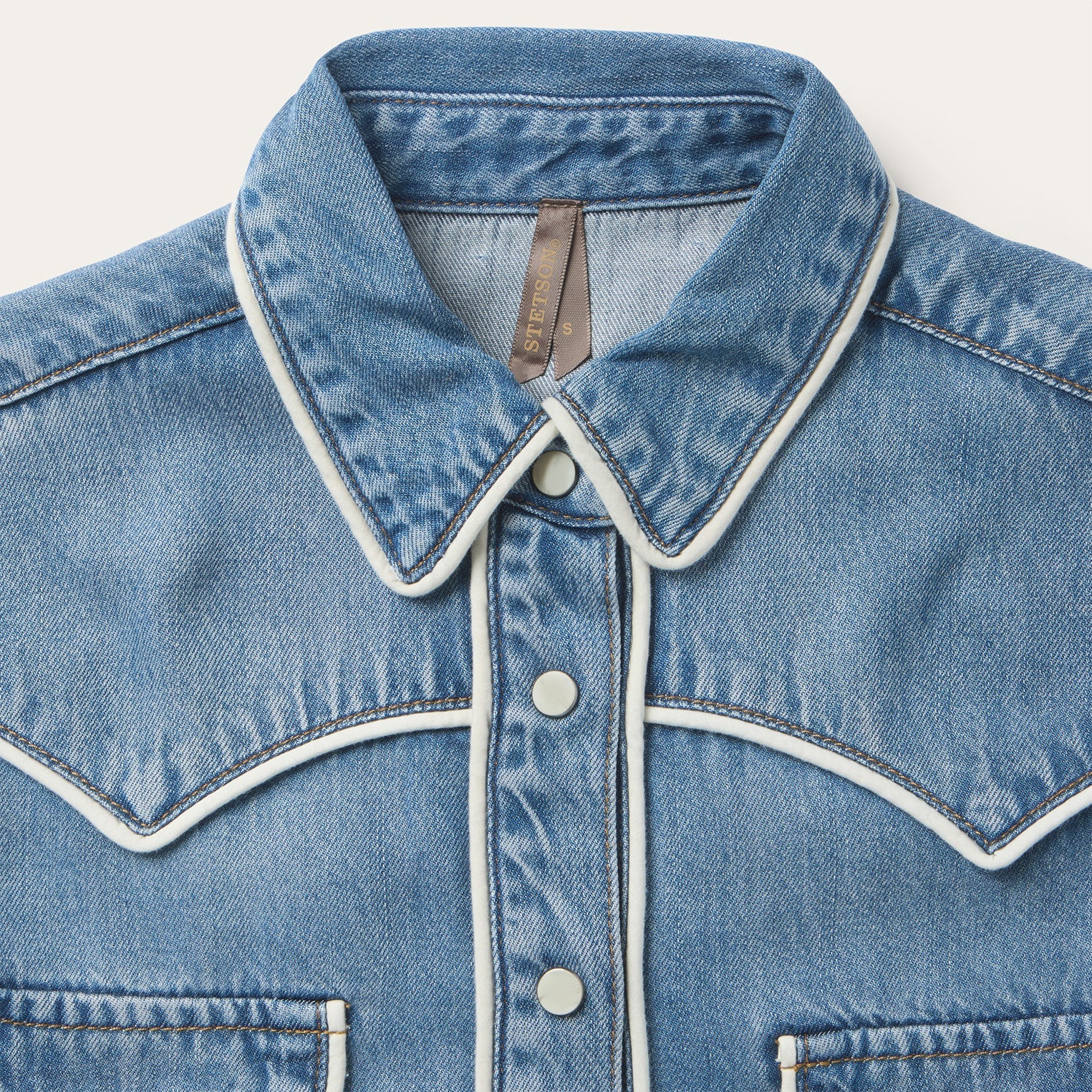 Close-up of a blue denim jacket with white trim on a light gray background