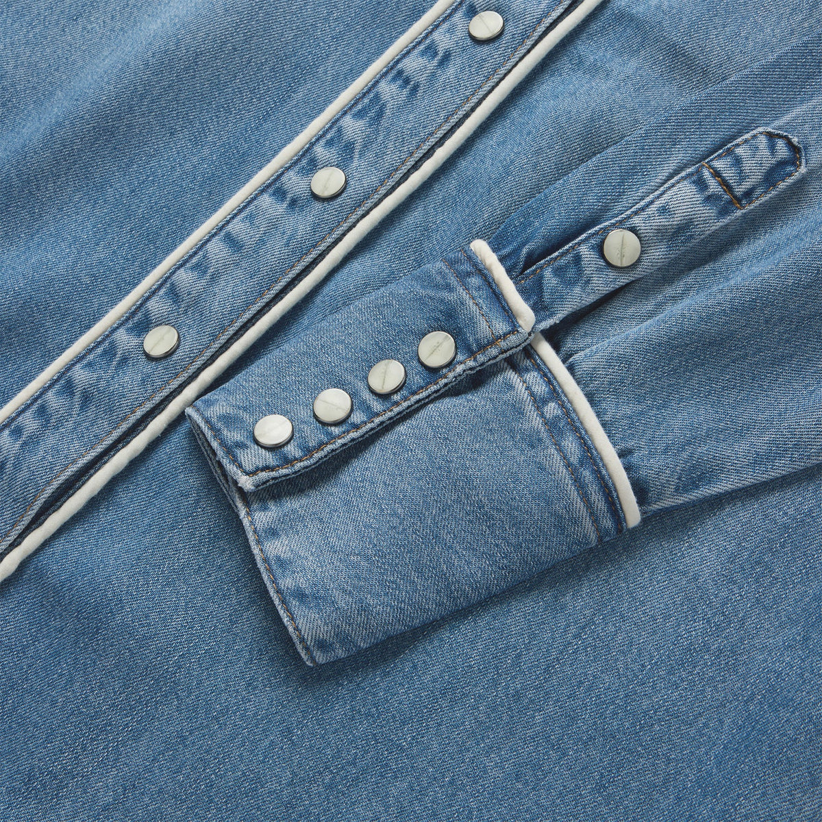 Close-up of a blue denim shirt with white trim and buttons.