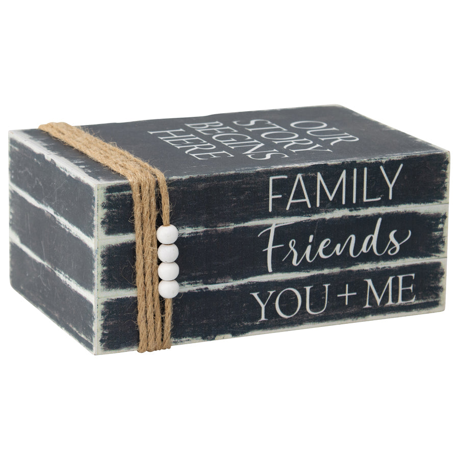 Our Story Begins Here Vintage Books with Beaded Tassel. Decorative wooden block with text 'Our Stories Here, Family, Friends, You + Me' on a white background