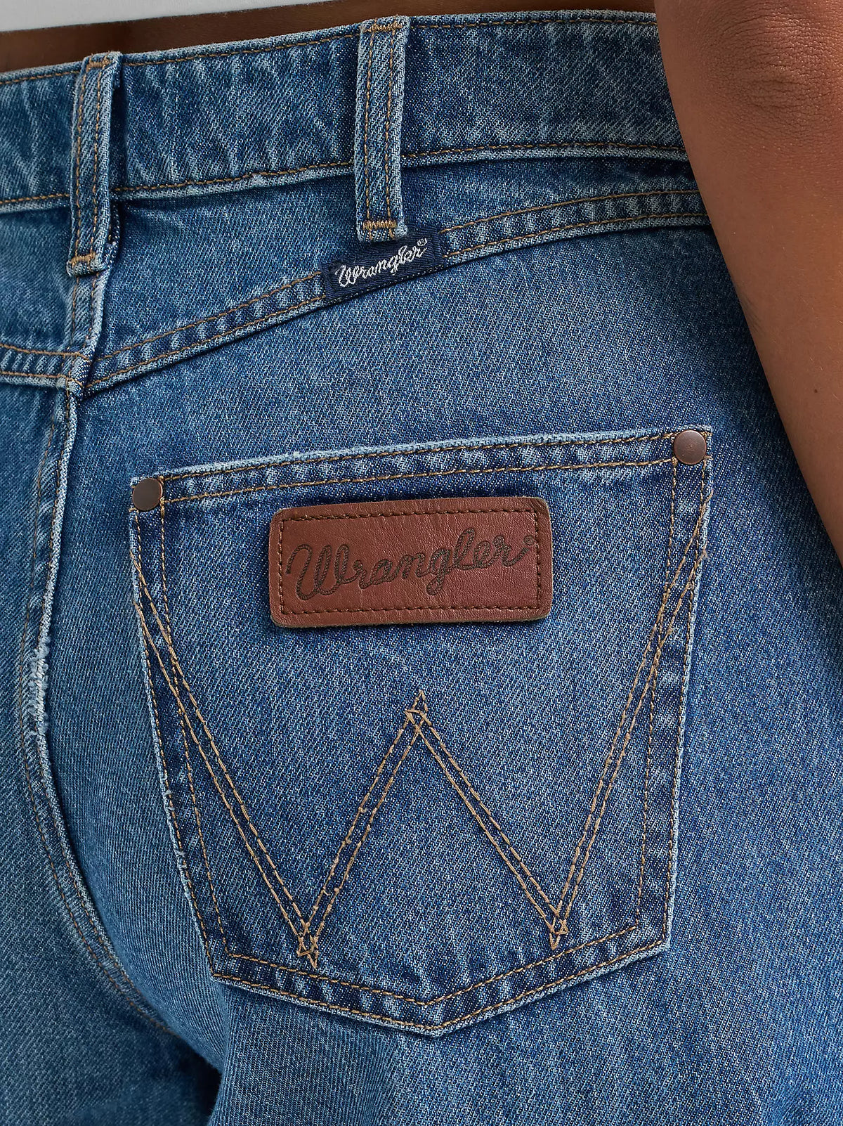 Close-up of a blue denim pocket with a Wrangler logo on a person wearing jeans.