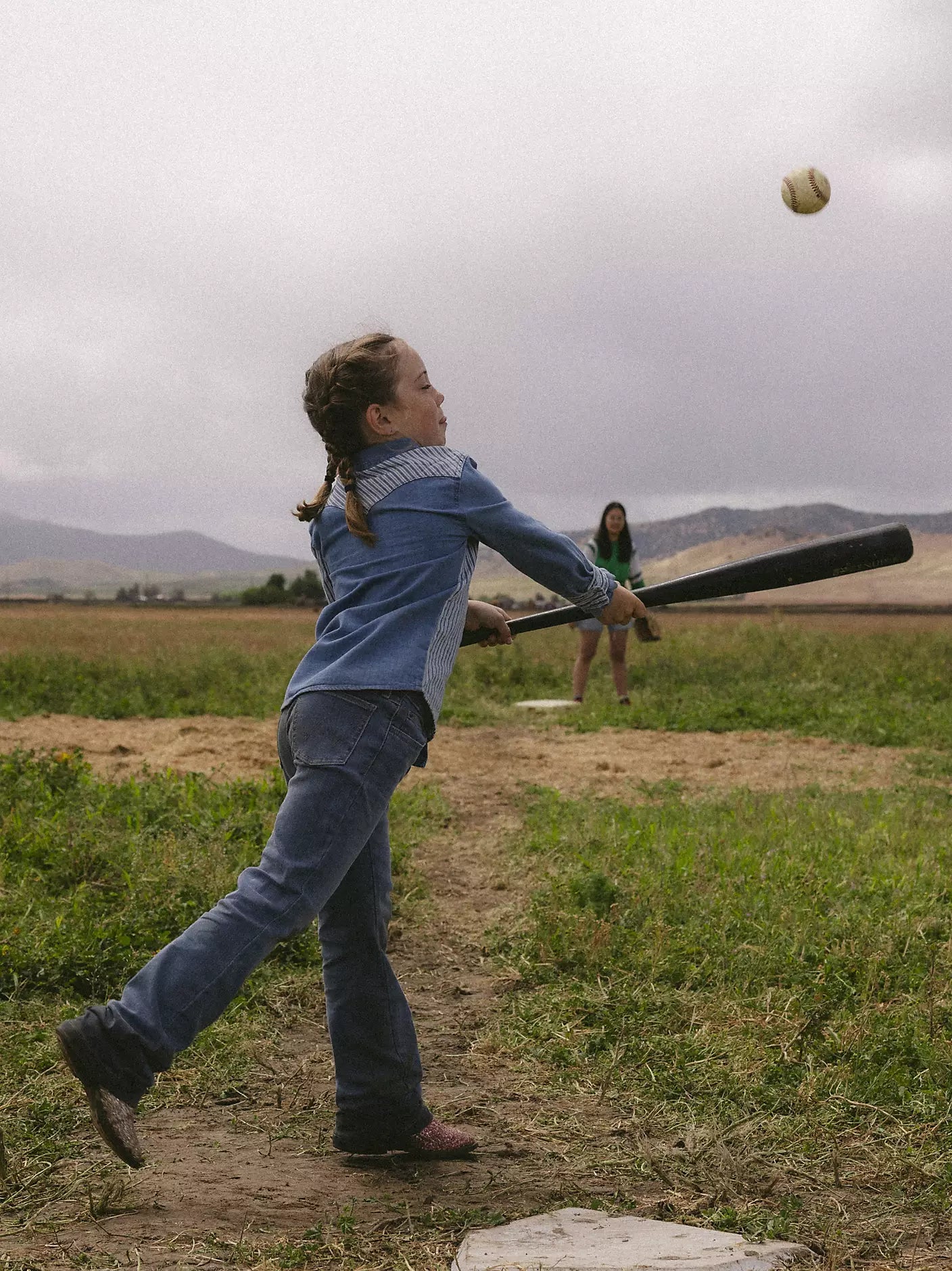 Child playing baseball in a field with another person in the background