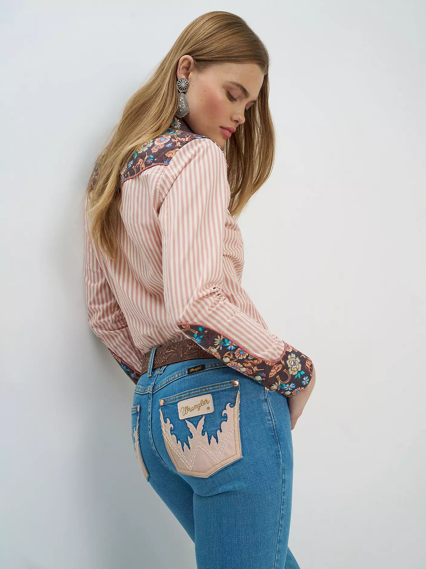 Woman wearing a patterned blouse and blue jeans against a white background