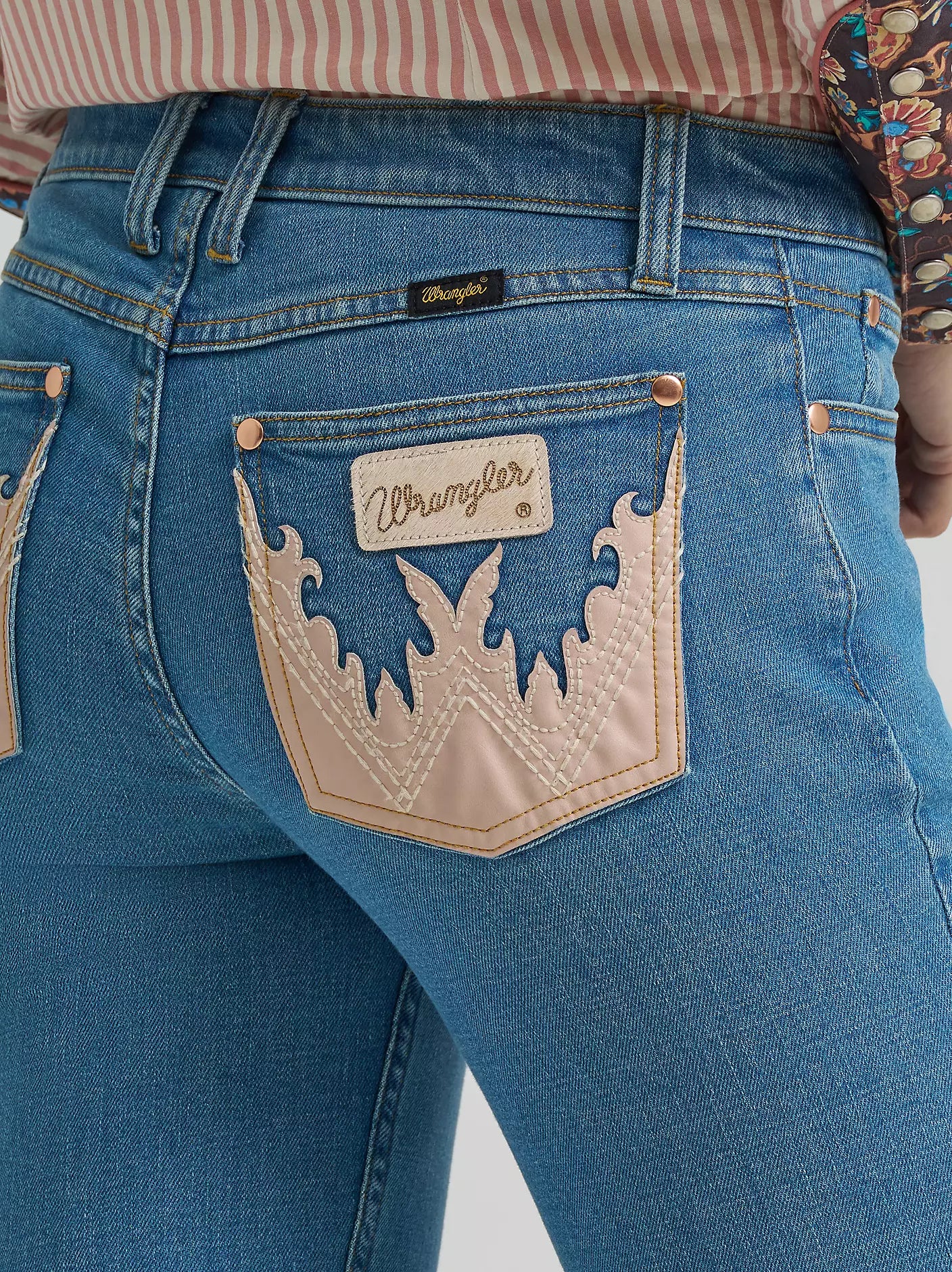 Close-up of blue jeans with a Wrangler logo on the pocket against a neutral background