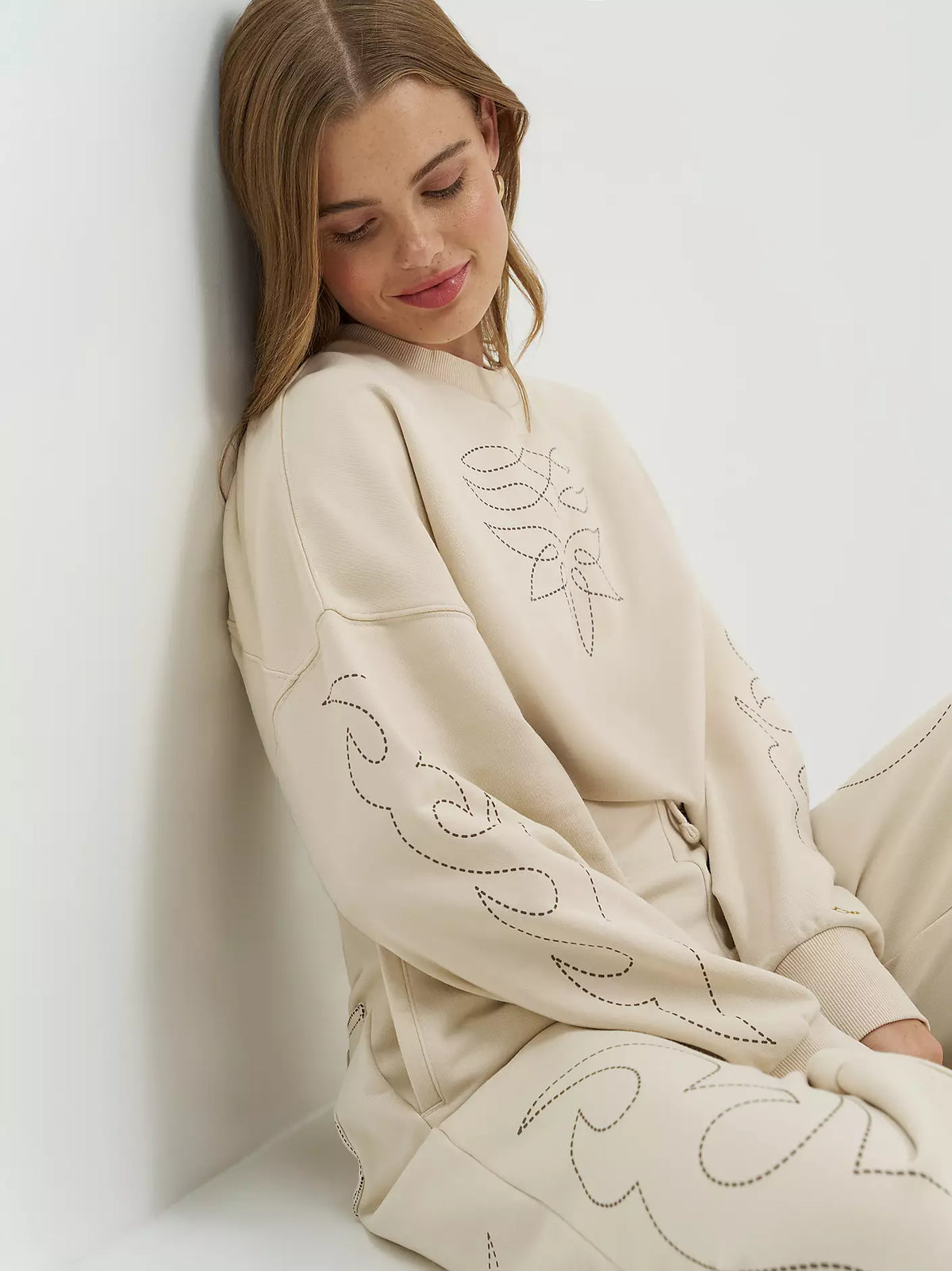 Woman wearing a cream-colored outfit with intricate patterns against a white background
