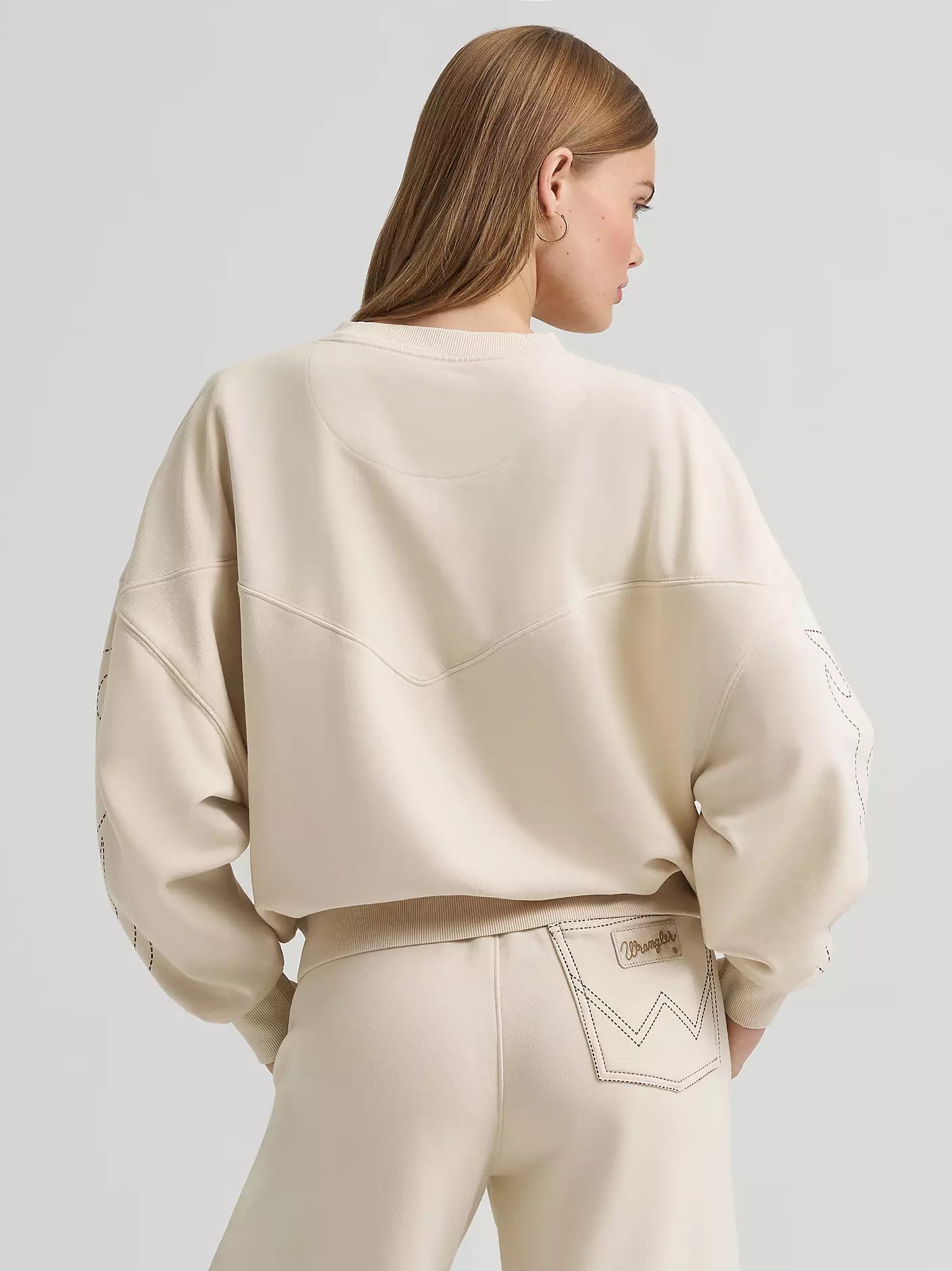 Person wearing a beige sweatshirt and pants on a light gray background