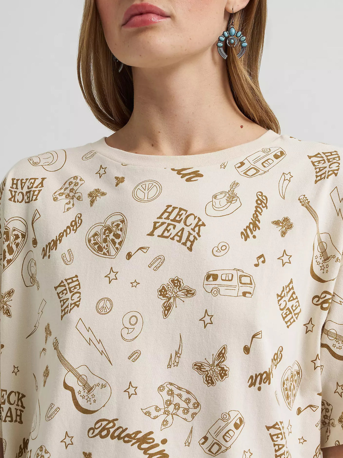 Person wearing a white shirt with brown graphic designs and text.