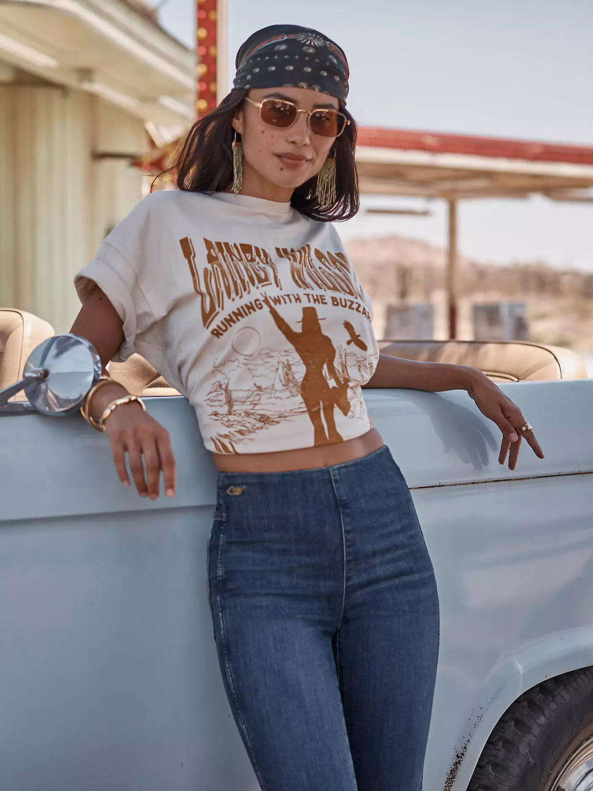 Woman wearing a graphic t-shirt and jeans leaning on a vintage truck.