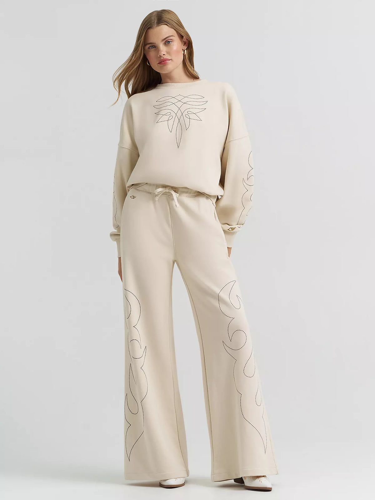 Woman wearing a beige outfit with floral embroidery on a light gray background