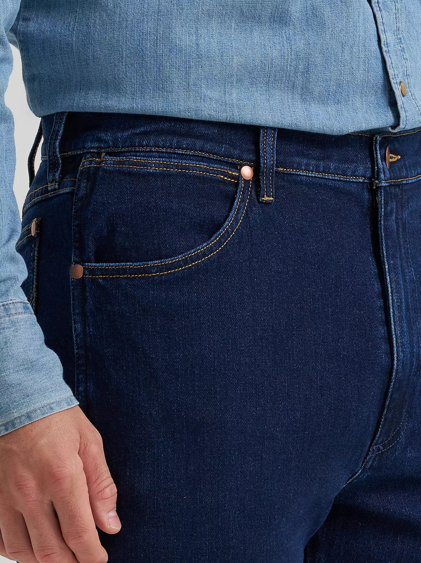 Close-up of a person wearing dark indigo denim jeans with a light blue denim shirt tucked in, showing the back pocket and waistband details.