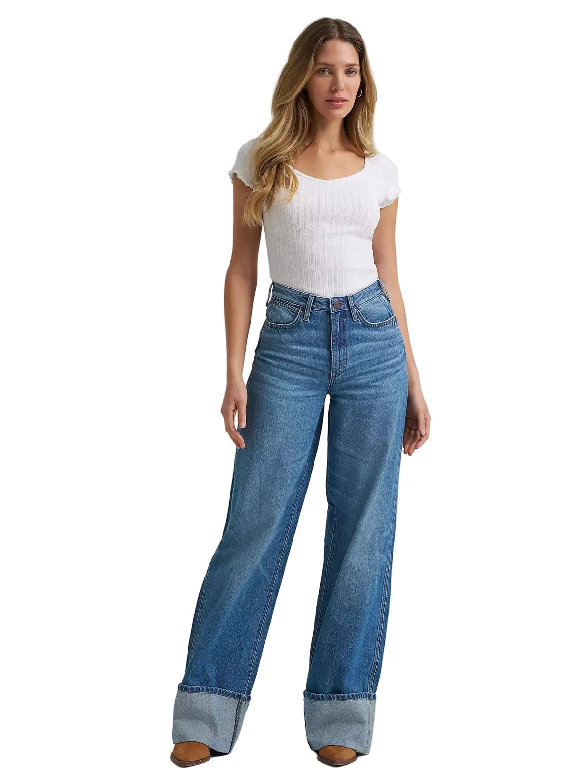 A woman modeling a pair of high-waisted, wide-leg blue jeans with rolled cuffs, paired with a white ribbed short-sleeve top, against a light gray studio background.