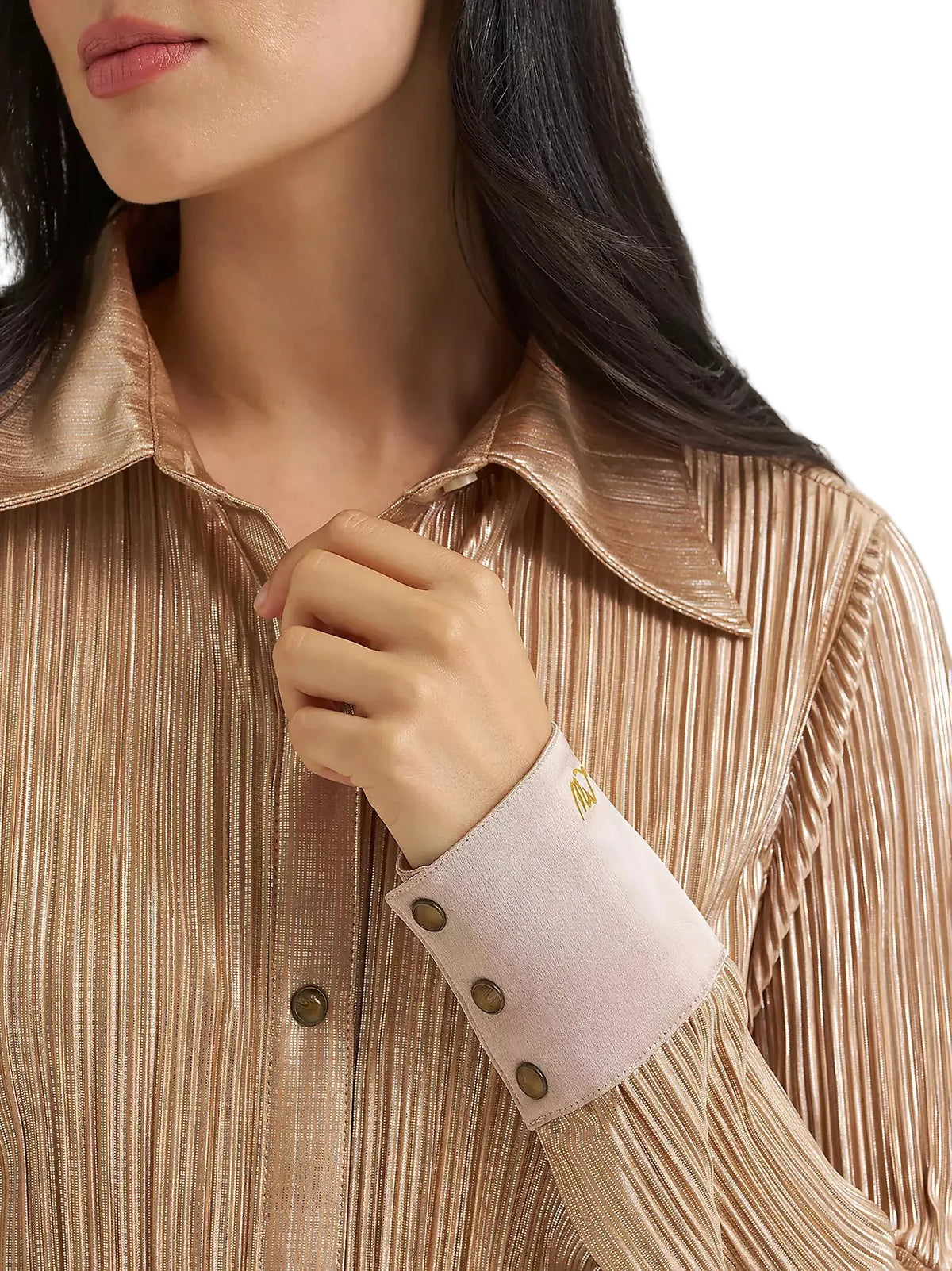 Close-up of a woman wearing a metallic champagne pleated button-down shirt with a contrasting light pink cuff and gold buttons.