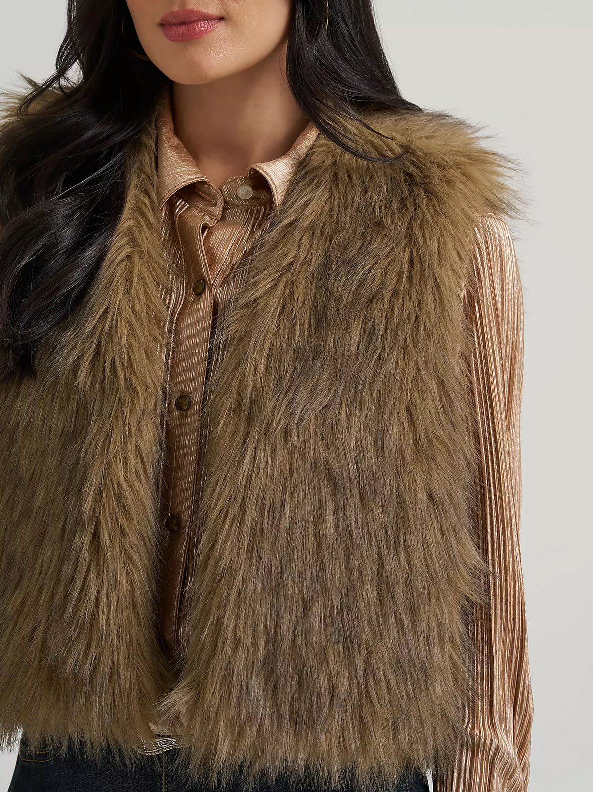 A close-up of a model wearing a brown faux fur vest over a pleated champagne-colored blouse.