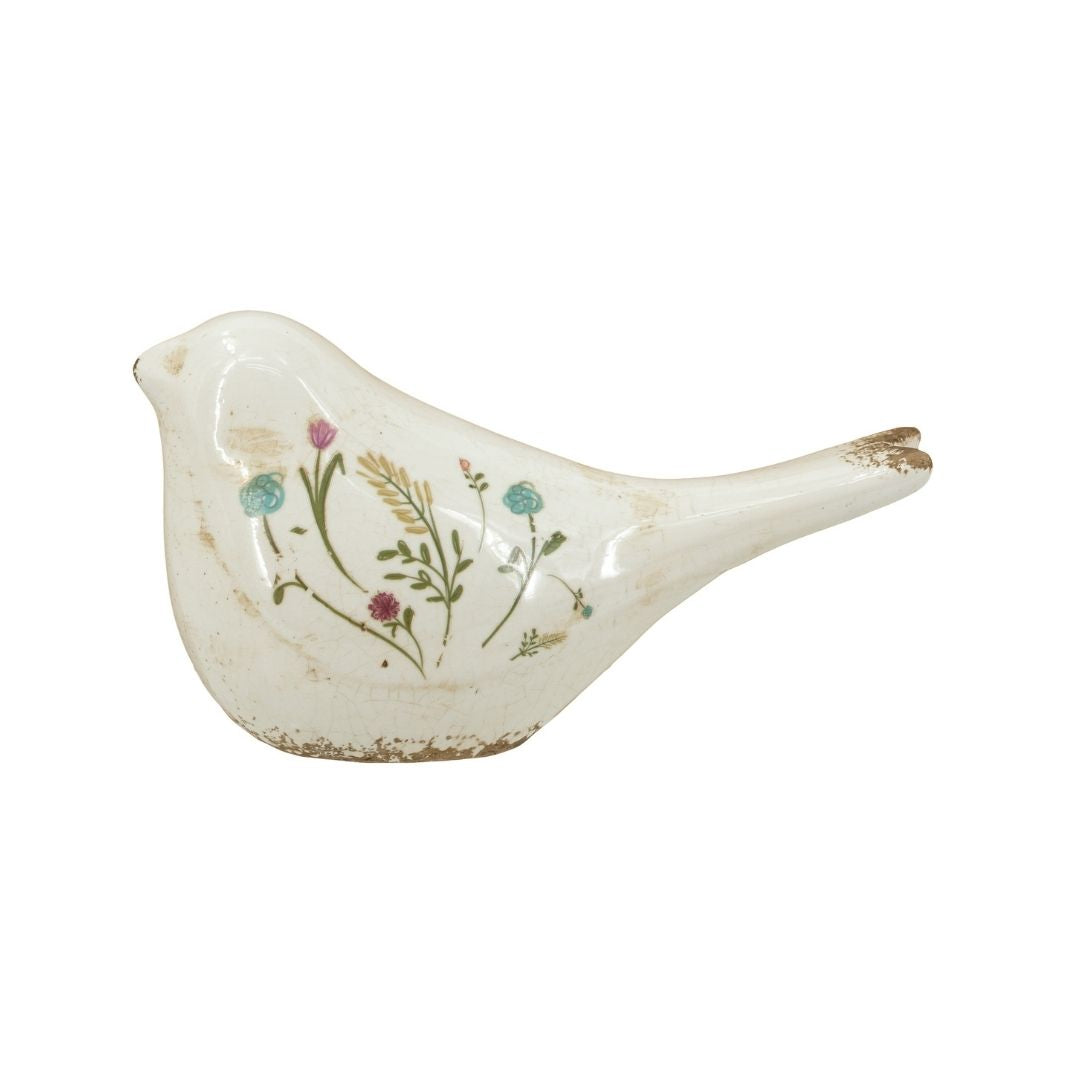 A decorative ceramic bird figurine with a distressed white glaze, decorated with delicate hand-painted wildflowers in green, pink, blue, and yellow, set against a plain white background.