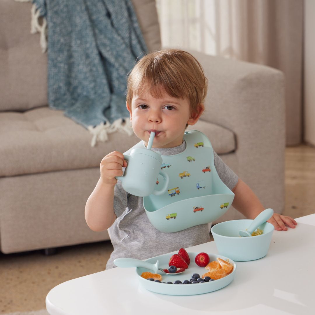 Child eating a meal with a bib and utensils in a home setting