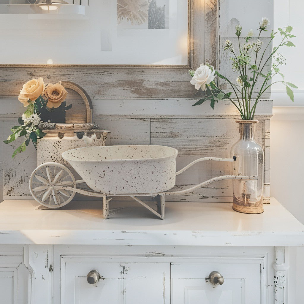 A decorative white speckled wheelbarrow-style planter or tray displayed on a white cabinet in a rustic room setting, with flowers in vases and a distressed wood wall behind it.