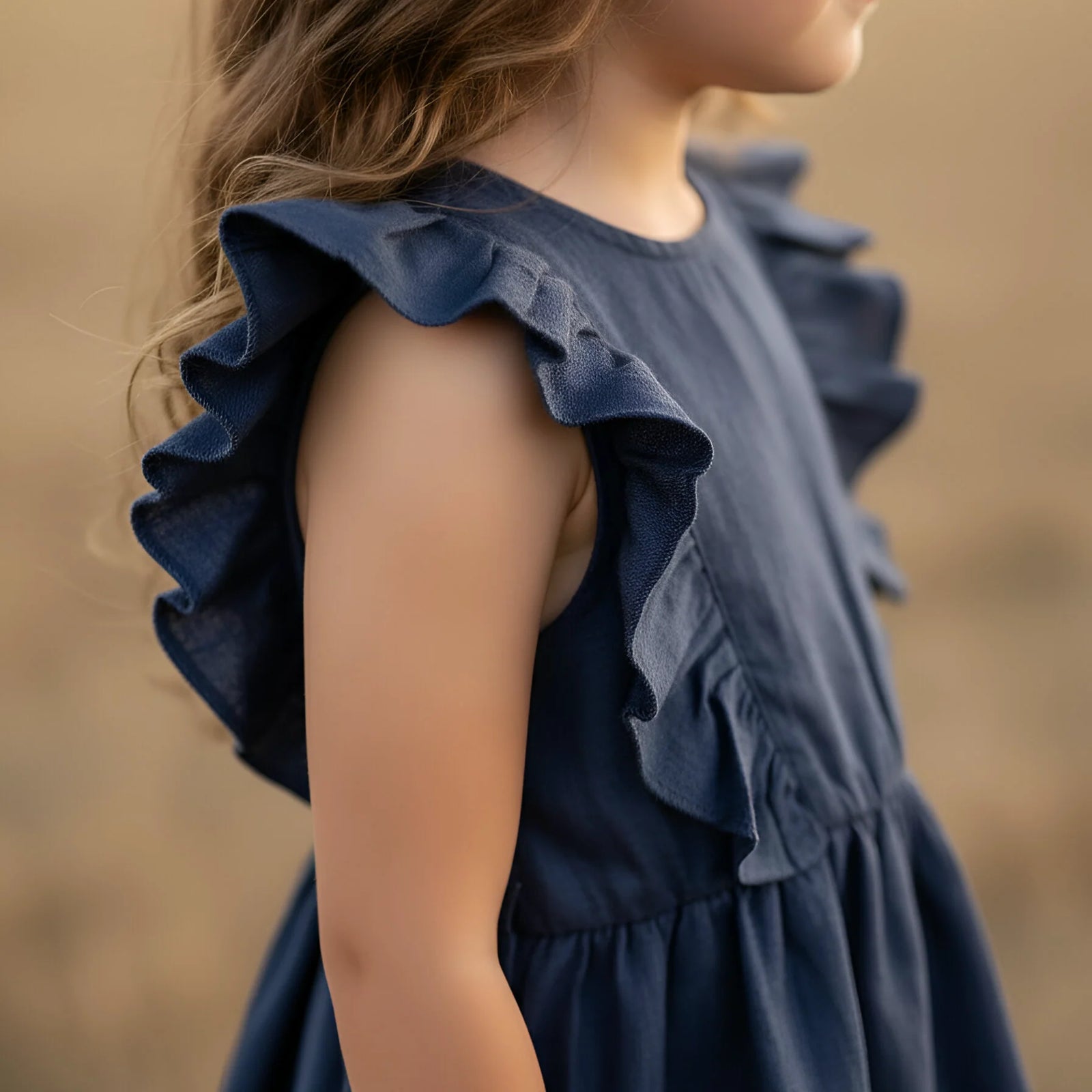 Young girl in a blue dress standing in a field during sunset.