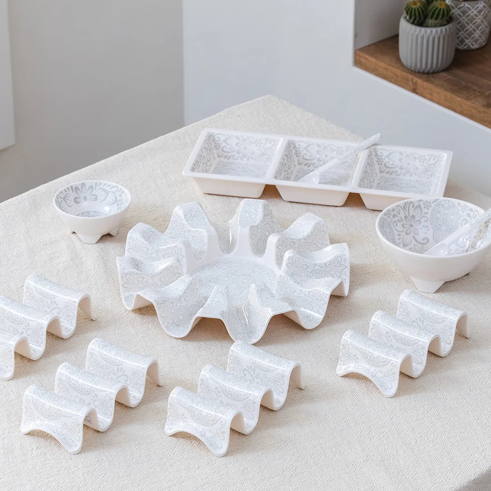 A white ceramic dinnerware set with a textured, embossed floral pattern, arranged on a beige linen tablecloth. The set includes a large ruffled platter, two small bowls with spoons, a three-compartment tray, and multiple wavy serving dishes.