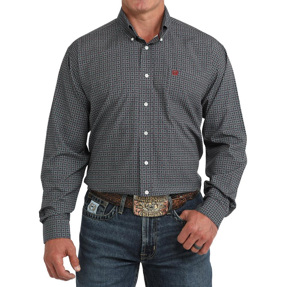 A man wearing a dark gray and black micro-patterned long-sleeve button-down shirt with white buttons, paired with blue jeans and a western belt.
