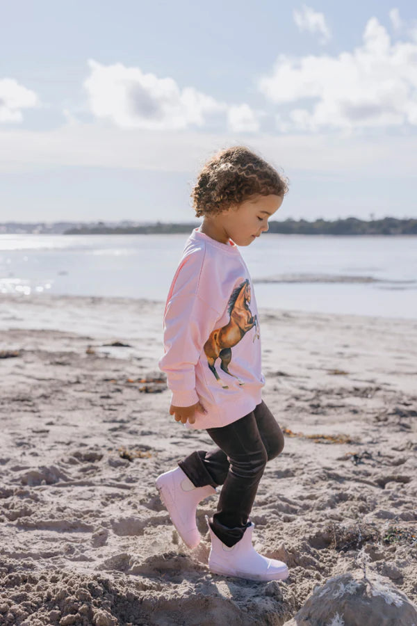 Child wearing a pink sweatshirt with a horse graphic on a beach