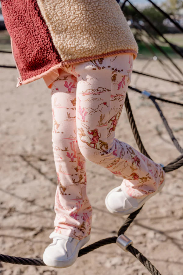 Child wearing patterned leggings and a red and beige jacket on a playground.