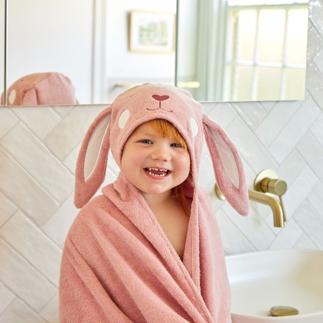 Child wearing a pink bunny robe and hat in a bathroom.