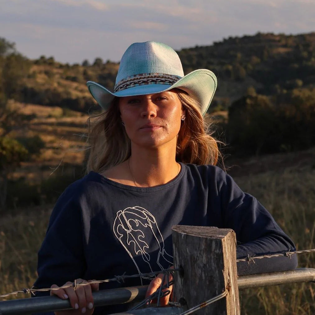 Woman wearing a blue cowboy hat and navy sweatshirt with a bear design, standing outdoors.